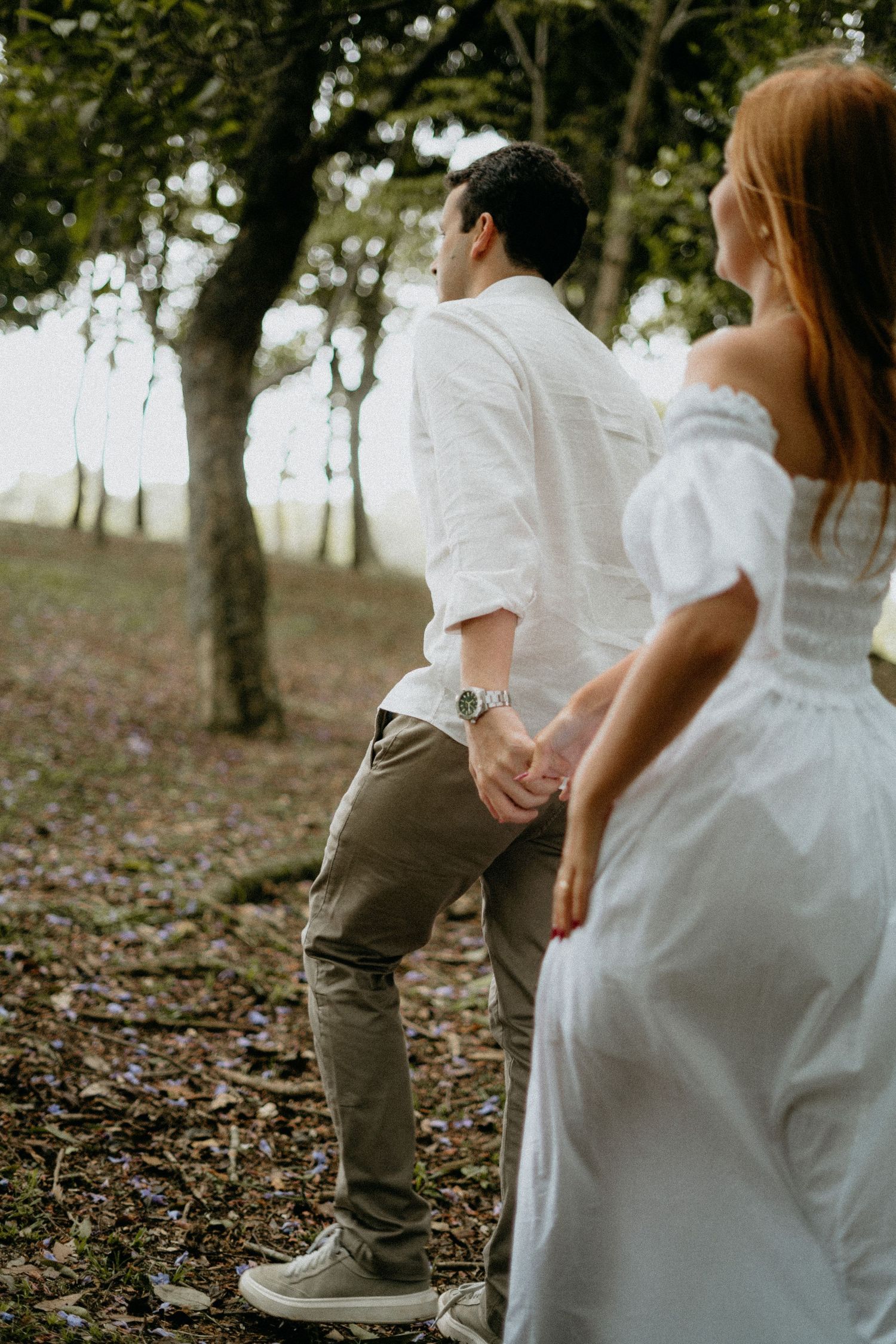 Couple stands among fallen leaves in white and neutral colored outfits during autumn engagement shoot.
