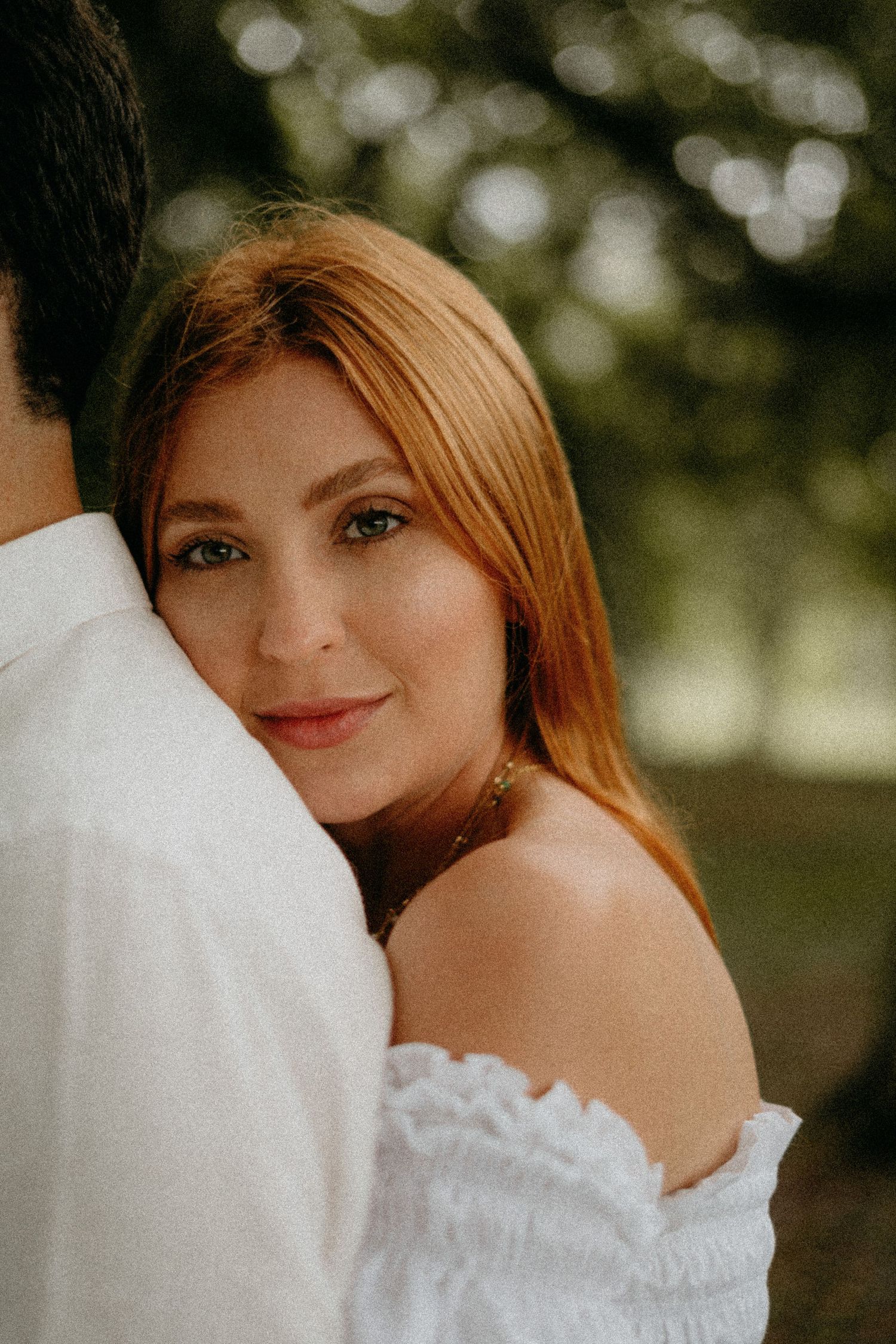 Woman in white off-shoulder dress poses for romantic outdoor portrait.