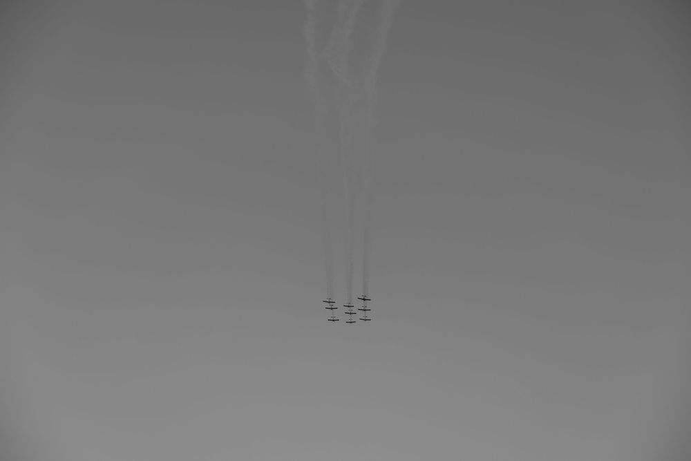 Formation of jets flying in sync leaving white smoke trails in a gray sky.