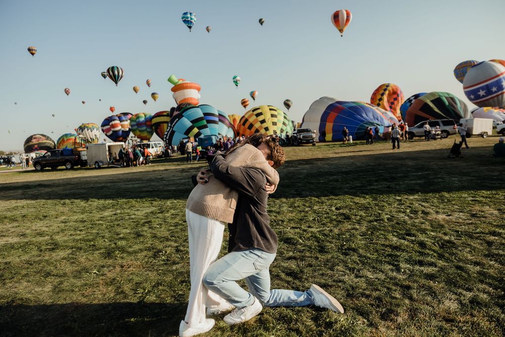 Joyful couple embracing and spinning at a vibrant hot air balloon festival outdoors.