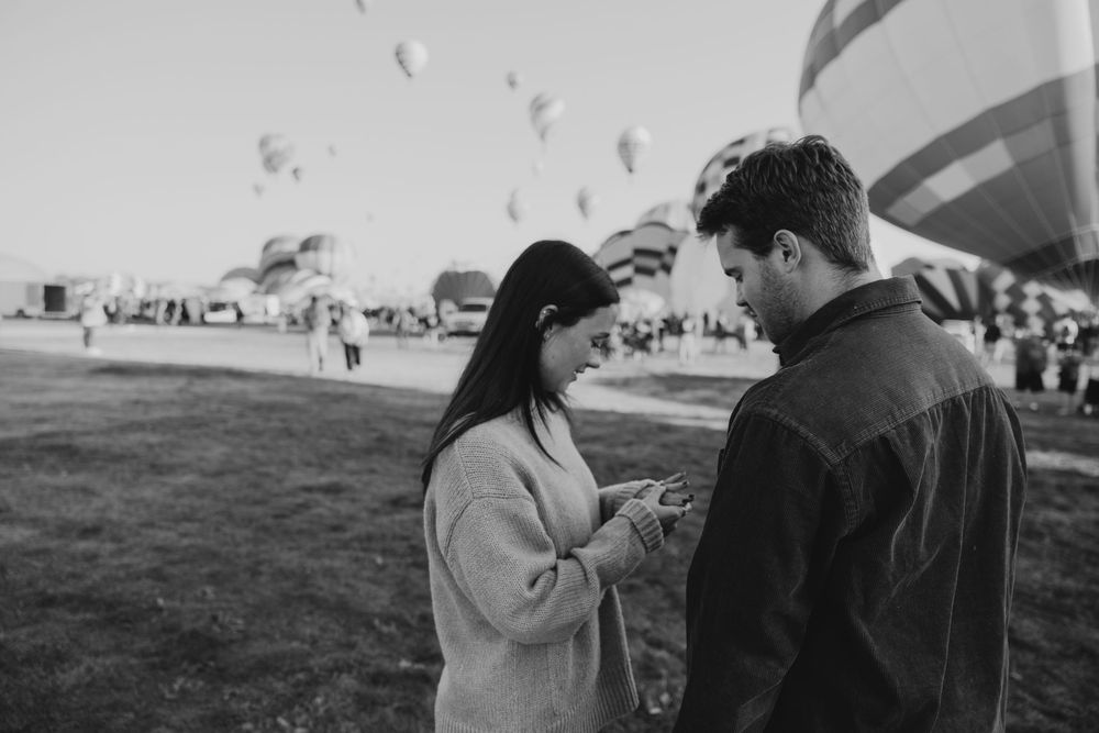 Black and white photo of couple looking at engagement ring at a hot air balloon festival.