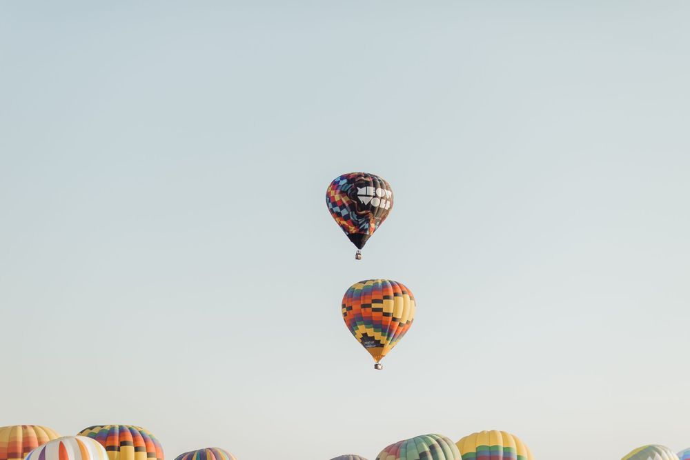 Two colorful hot air balloons soaring high in a clear sky above a festival field.