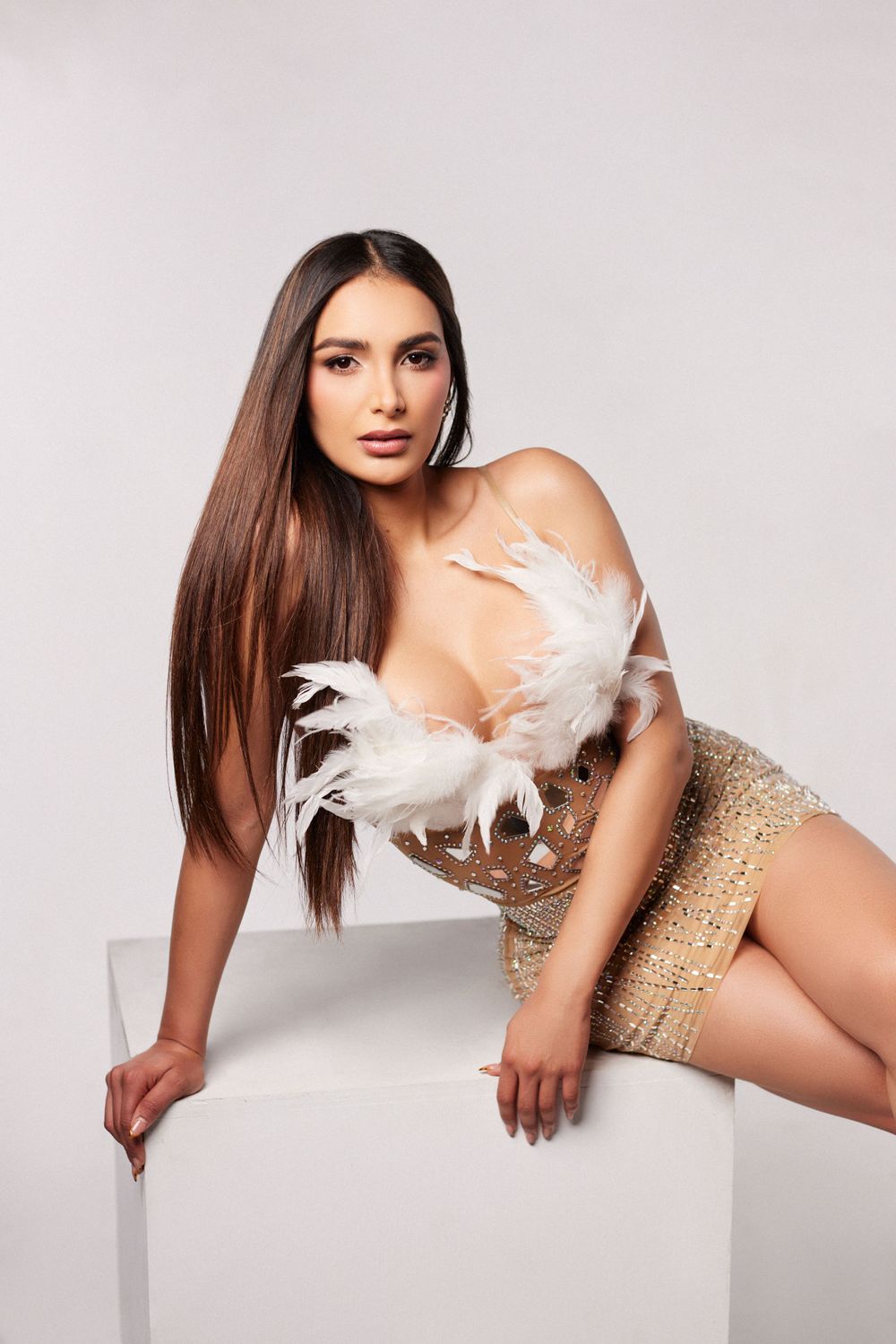Glamour photo series with white feathers and gold sequined outfit against light background.