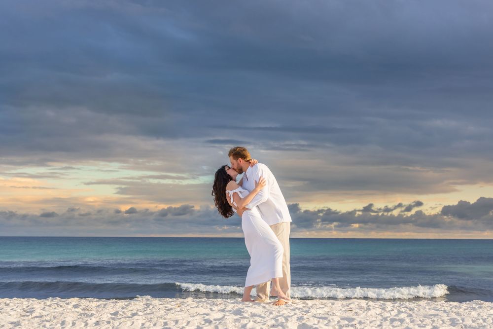 Couple walking hand in hand on white sandy beach at sunset as waves break along the shoreline.