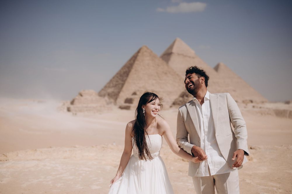A couple poses romantically in front of the ancient Egyptian pyramids of Giza during a desert photoshoot.