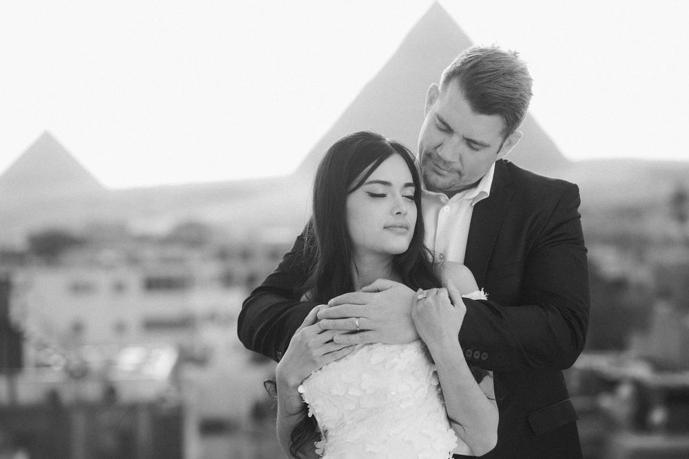 A romantic black and white photo of a couple embracing in front of the Egyptian pyramids in Giza.