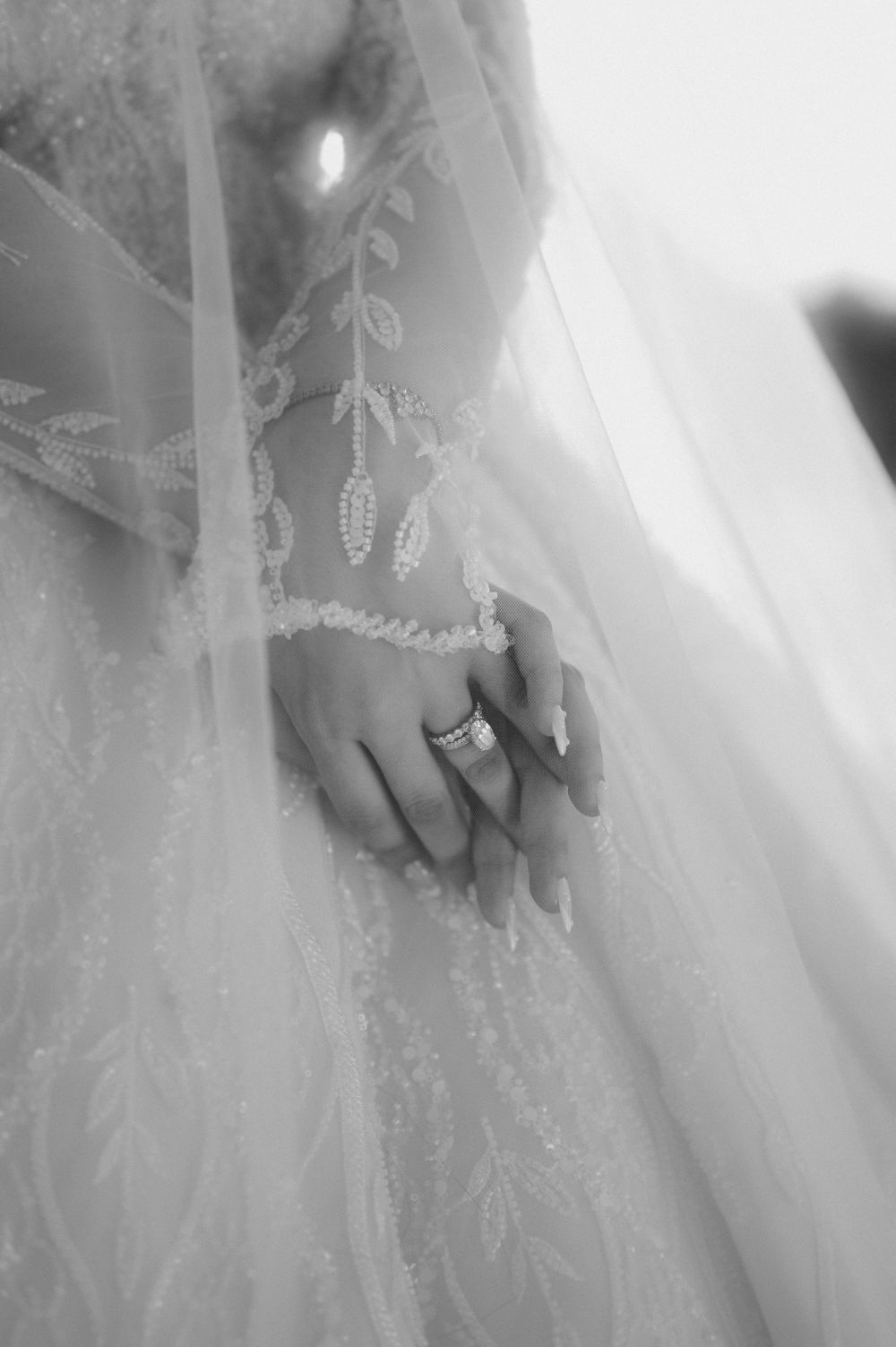Delicate white lace detailing on a wedding dress flowing down with a close-up of hands brushing against the fabric.