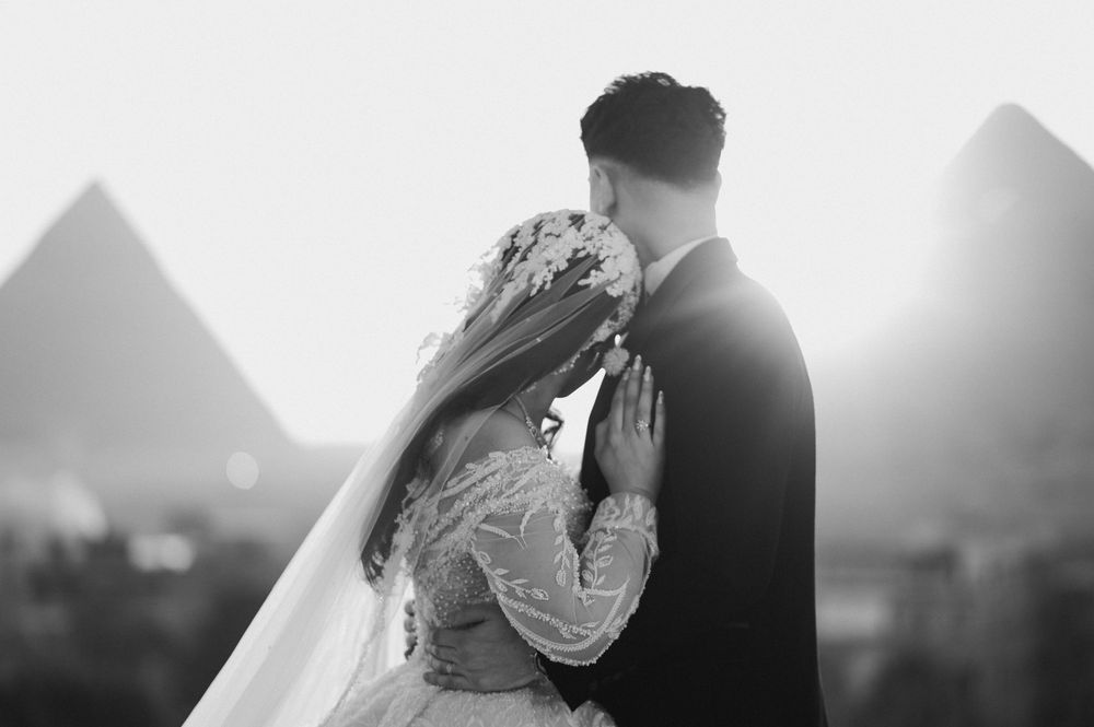 A black and white panoramic wedding photograph showing a couple walking against a cloudy sky backdrop.