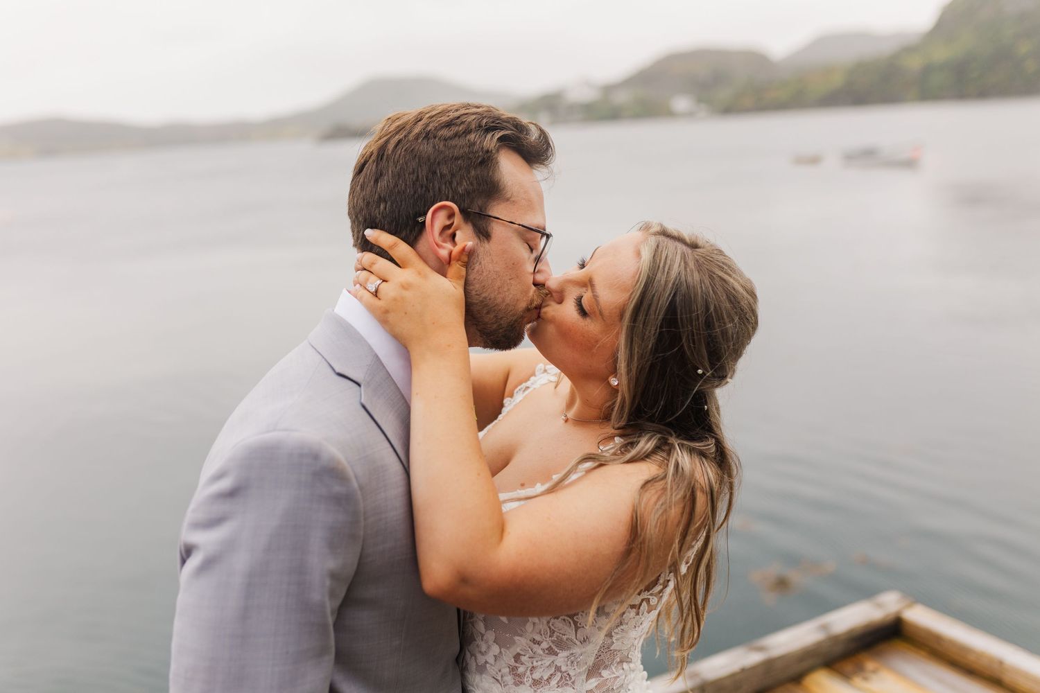 Romantic couple sharing tender kisses along a misty ocean shore with mountains in the background.