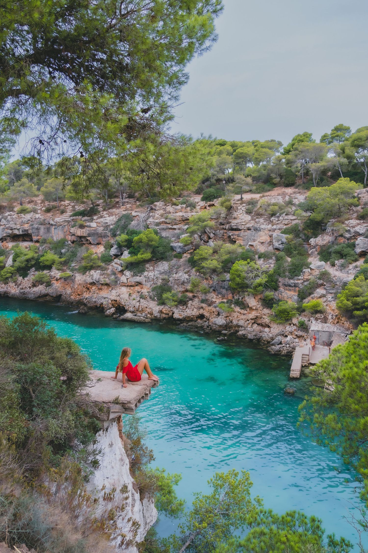 People enjoying crystal clear turquoise waters at a hidden cove surrounded by rocky cliffs and pine trees in Mallorca.