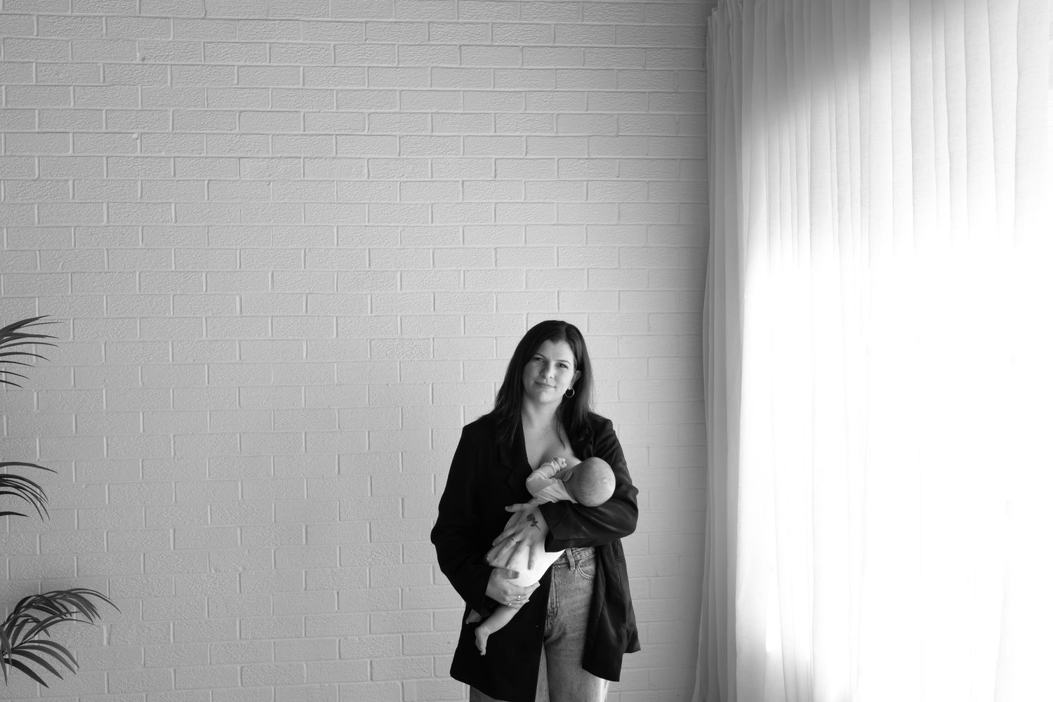 Milly from Photography by Milly stands heeding her newborn during a relaxed portrait session in a natural light studio.