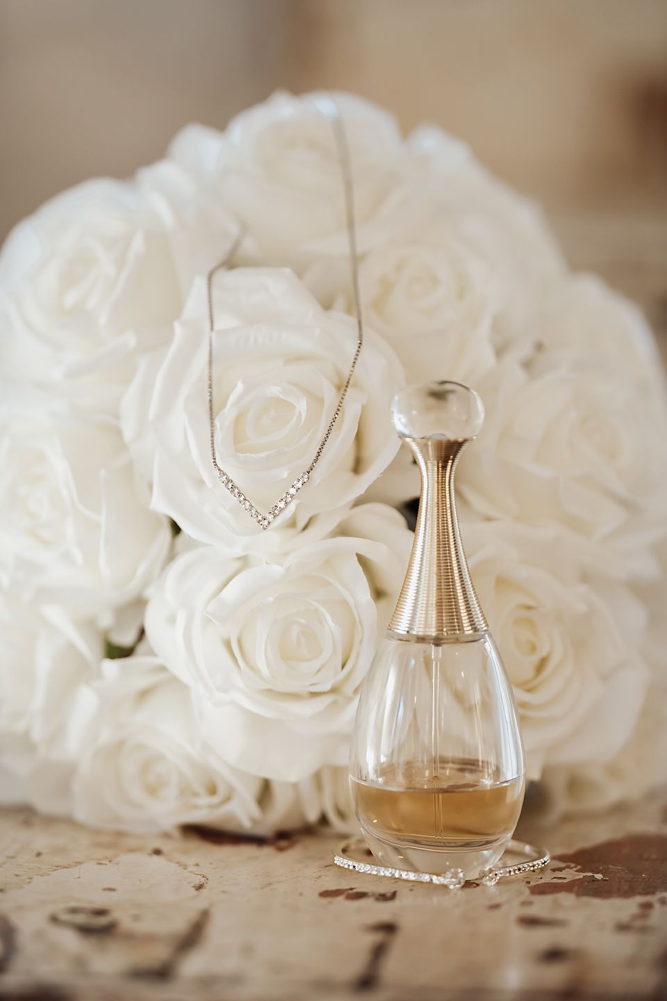 A delicate arrangement of white roses beside a perfume bottle on a textured surface in soft focus.
