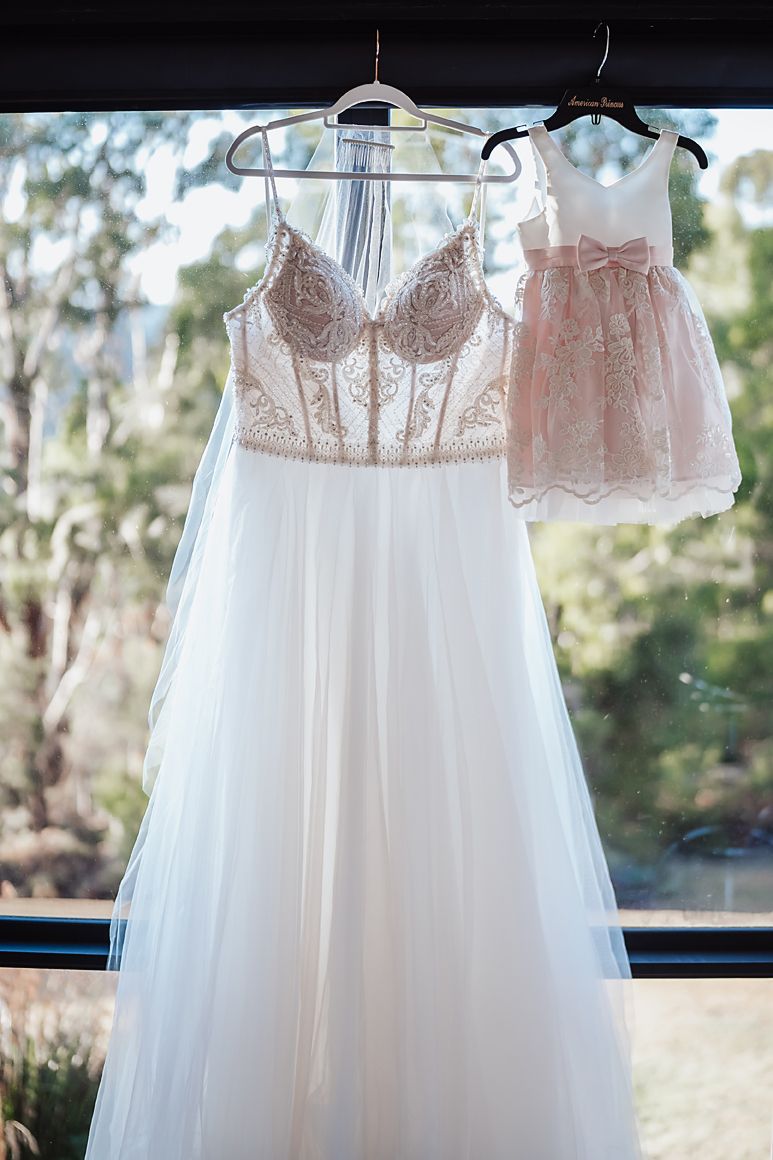 White lace wedding dresses hanging in a row against a bright window with trees visible outside.
