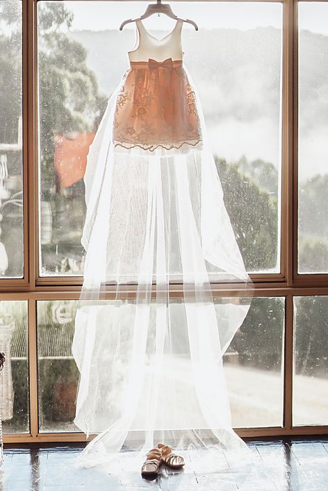 Wedding gown and veil hanging in window frame with natural light creating ethereal bridal display.