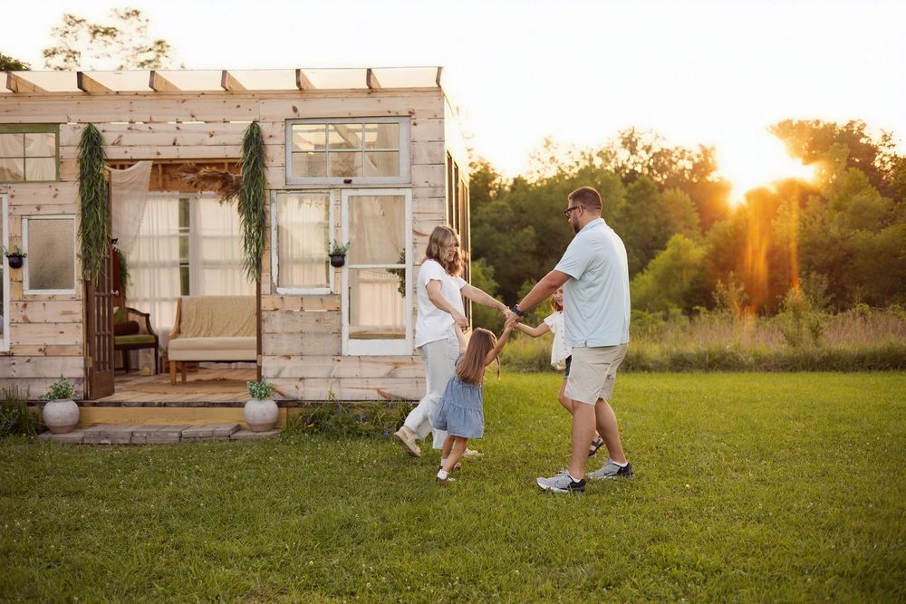 Couple dancing together on green grass at sunset in front of a rustic wooden tiny home.