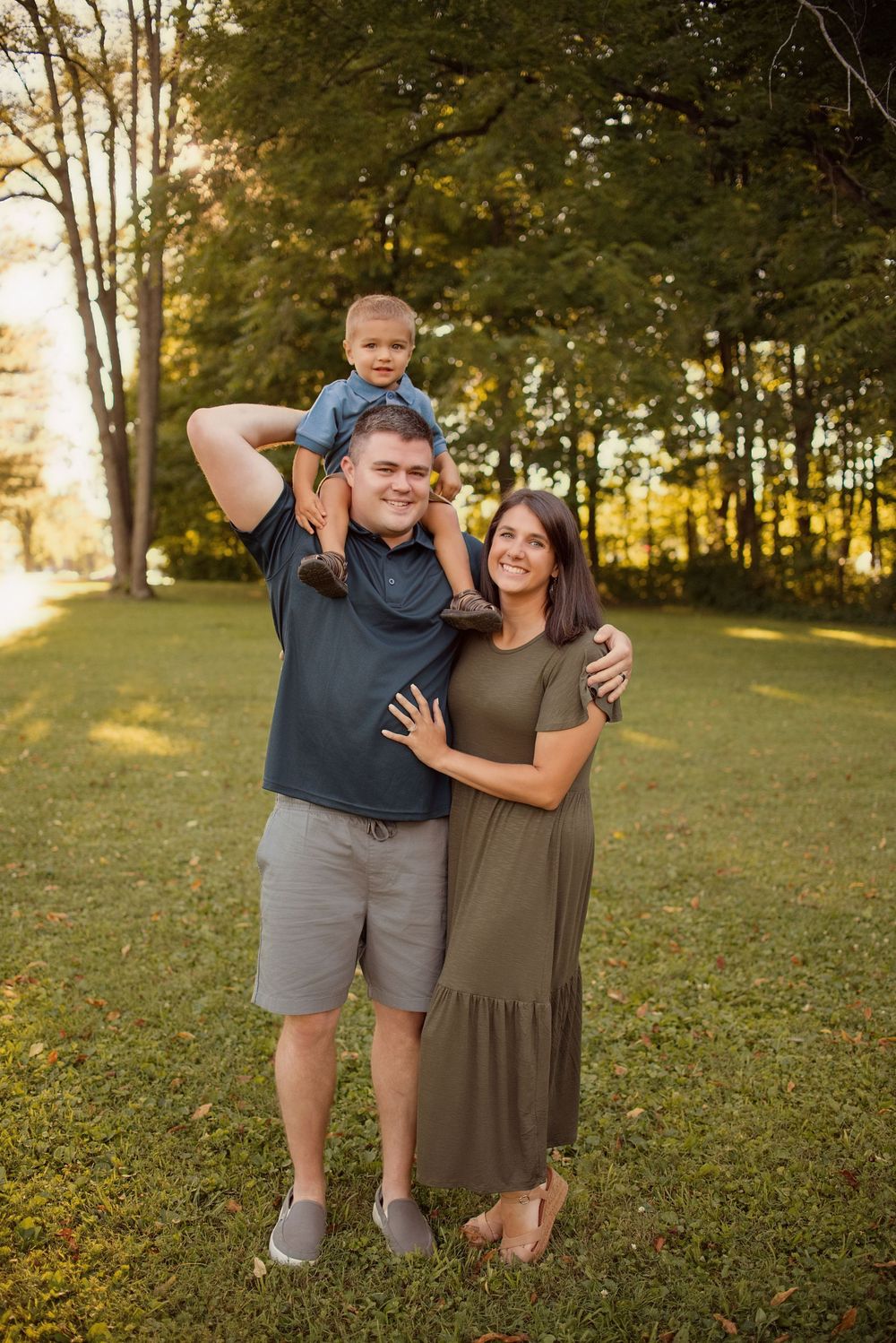 A family of three poses playfully together on a grassy hill during golden hour sunset.