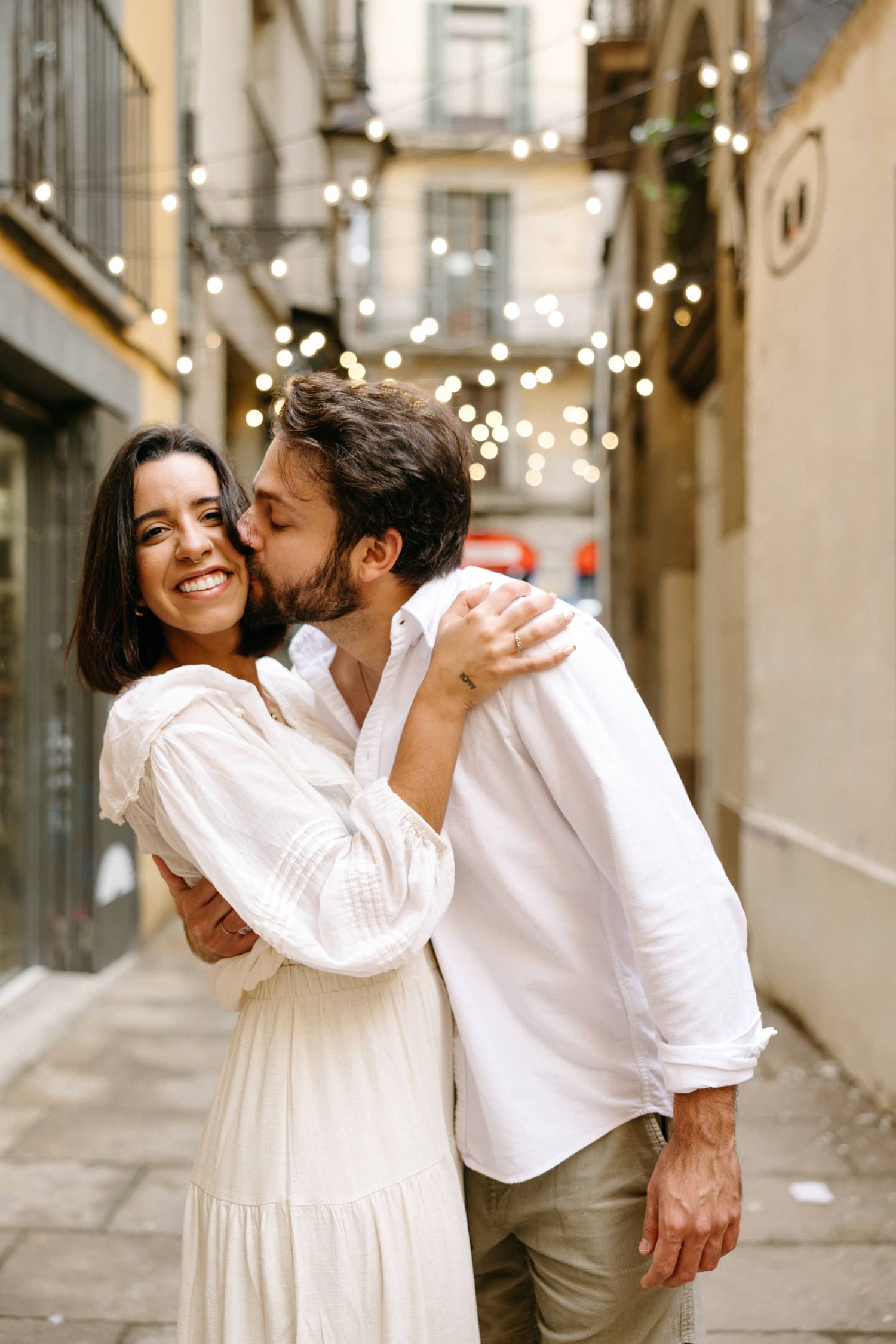 A joyful couple sharing an intimate moment in a narrow European street with twinkling lights.