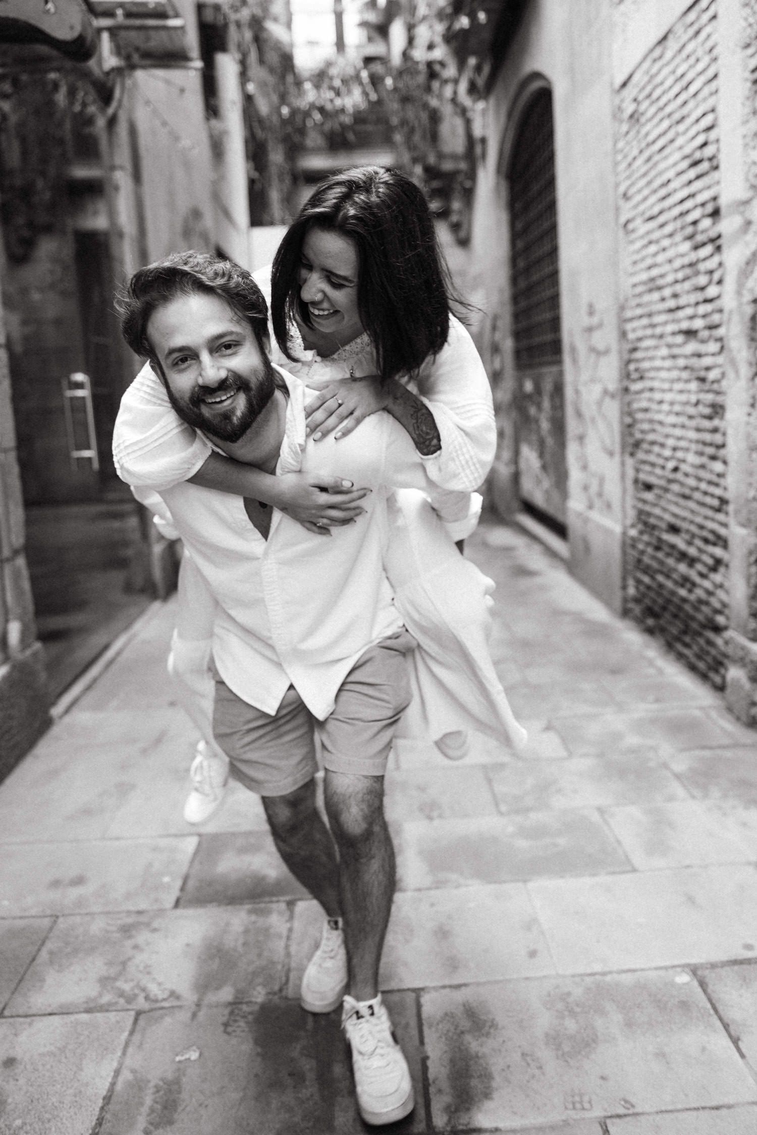 A playful black and white photo of a couple having fun in a historic stone alleyway.