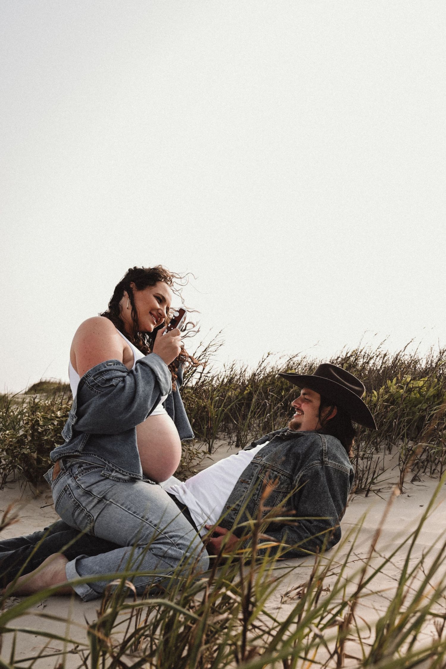 Casual maternity photoshoot on a beach with denim and natural lighting.