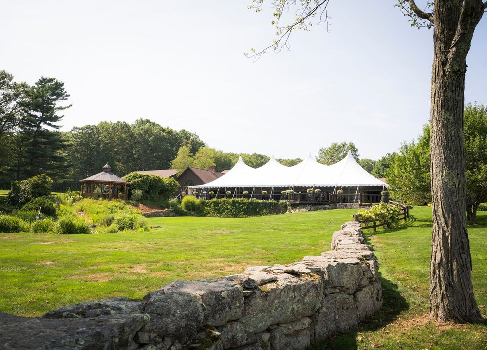 White wedding tent set up on a lush green lawn with a rustic stone wall in the foreground.