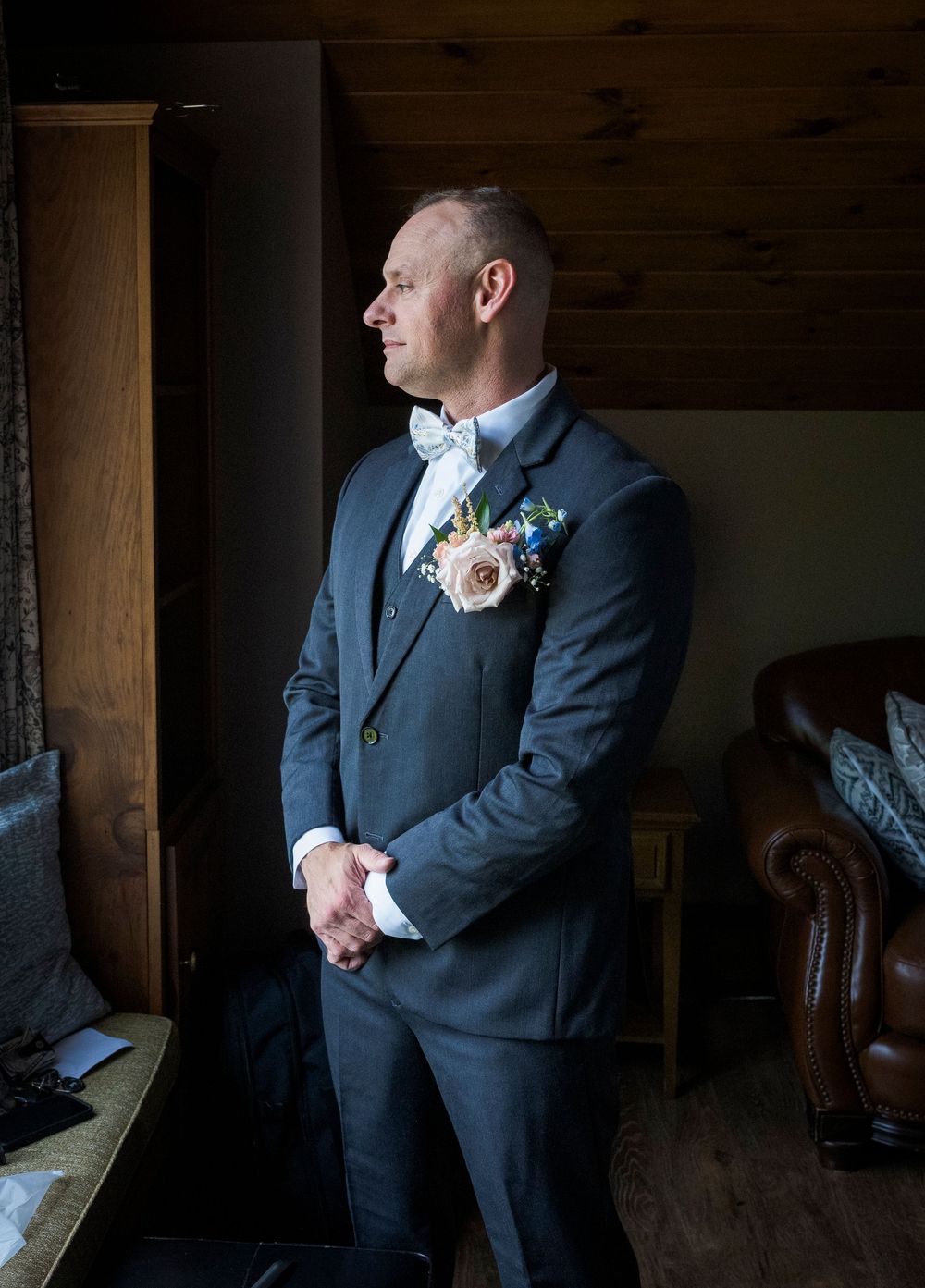 Artistic portraits of a groom in a dark wooden room with natural lighting.