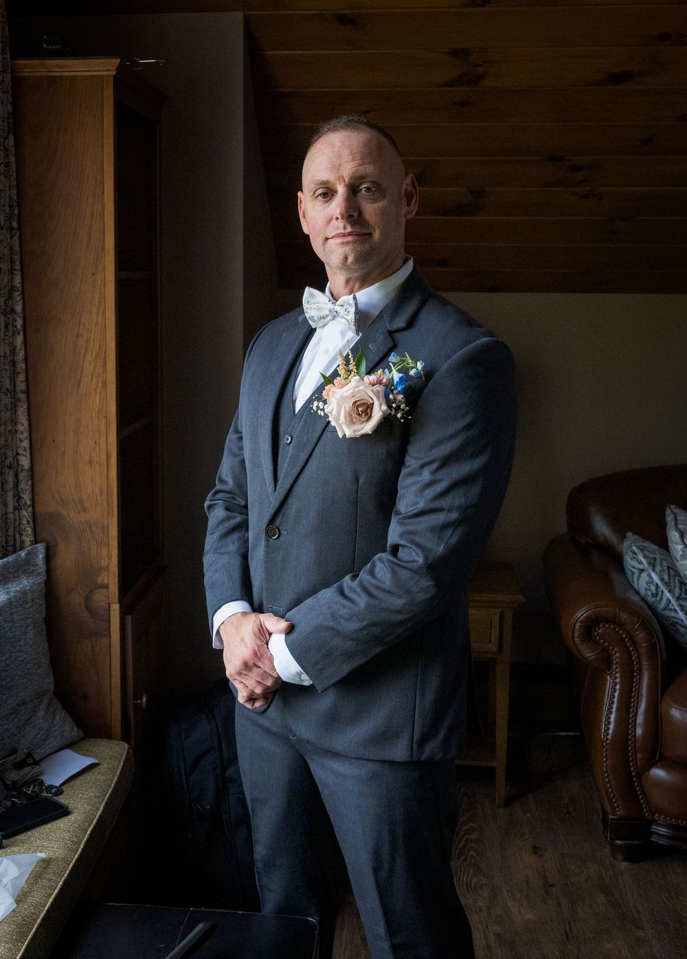 Groom in a grey suit with boutonniere posing in dramatic lighting indoors.