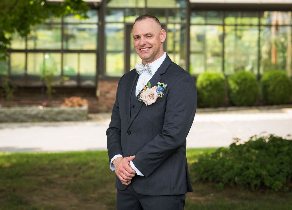 Wedding party members in formal attire posing outdoors in a scenic garden setting.