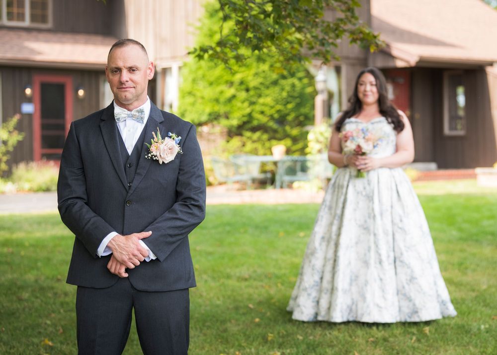 A wedding party poses outdoors in formal attire against a green lawn and building backdrop.