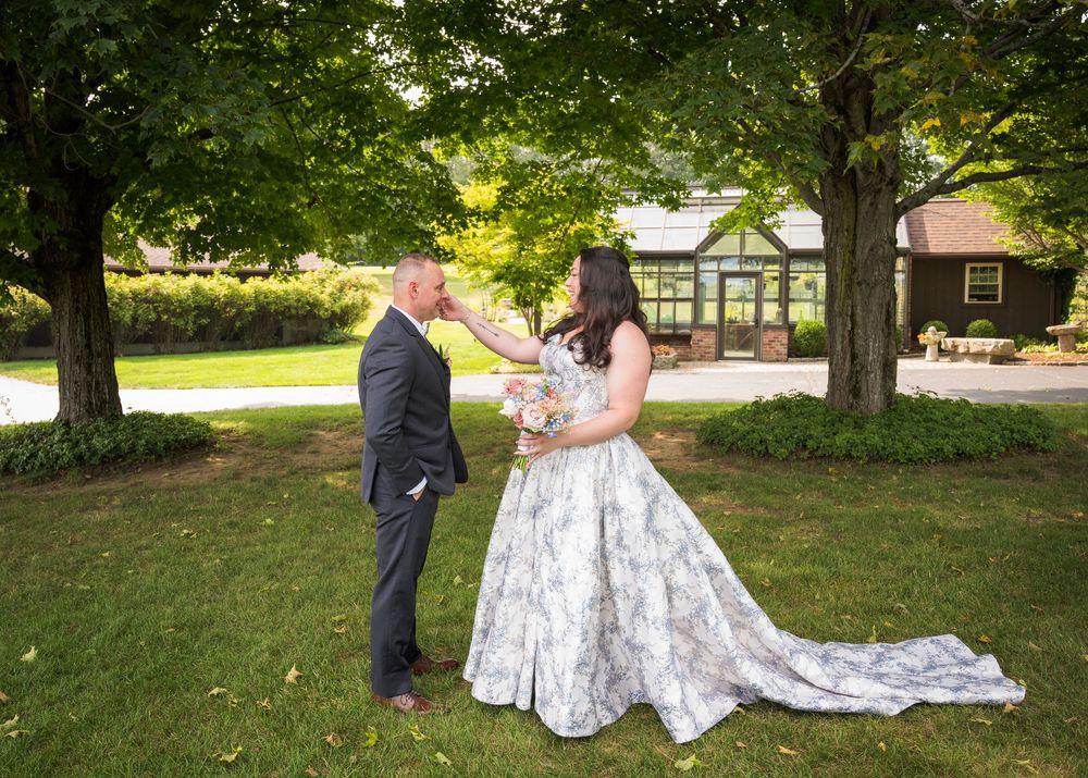 Bride in a floral dress and groom in dark suit taking romantic photos on a grassy lawn.