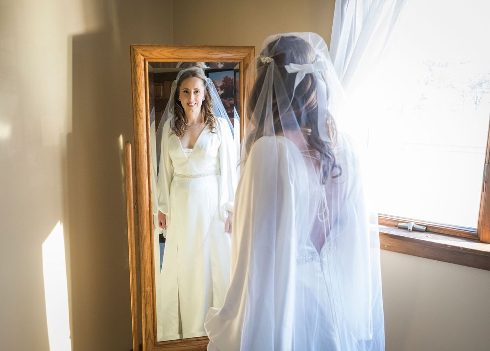 Sunlit bridal gown hanging by a window with soft natural light creating an ethereal glow.