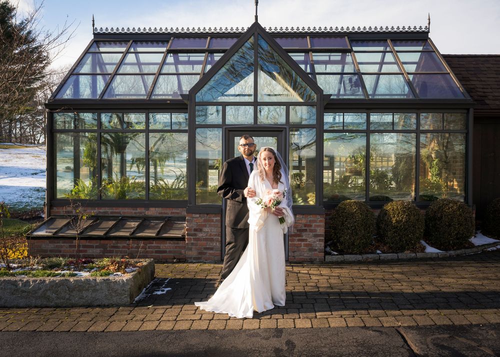 Modern glass greenhouse wedding venue with stone foundation and scenic mountain backdrop.