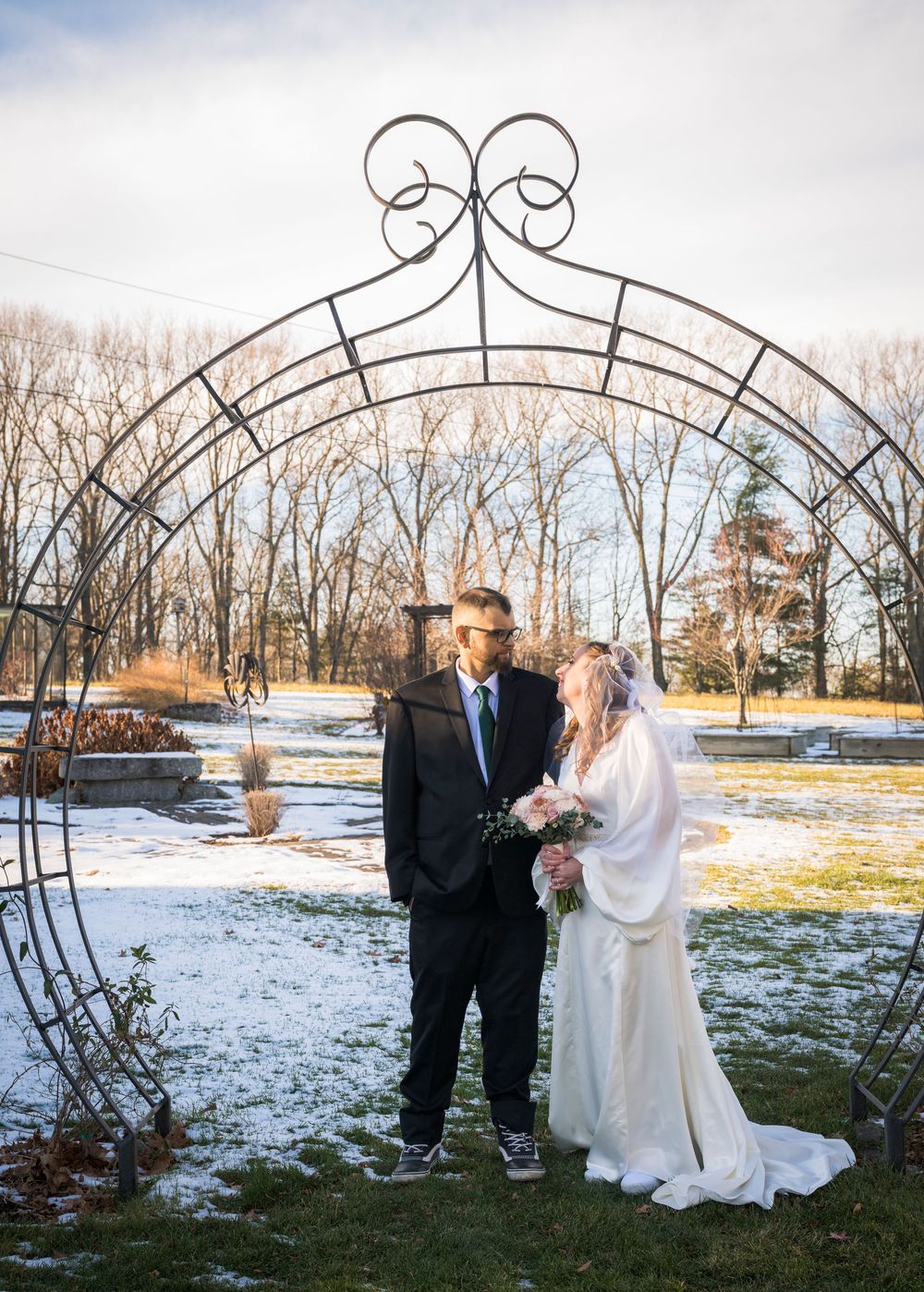 A winter wedding photo series showing a couple posing under a decorative metal arch in the snow.