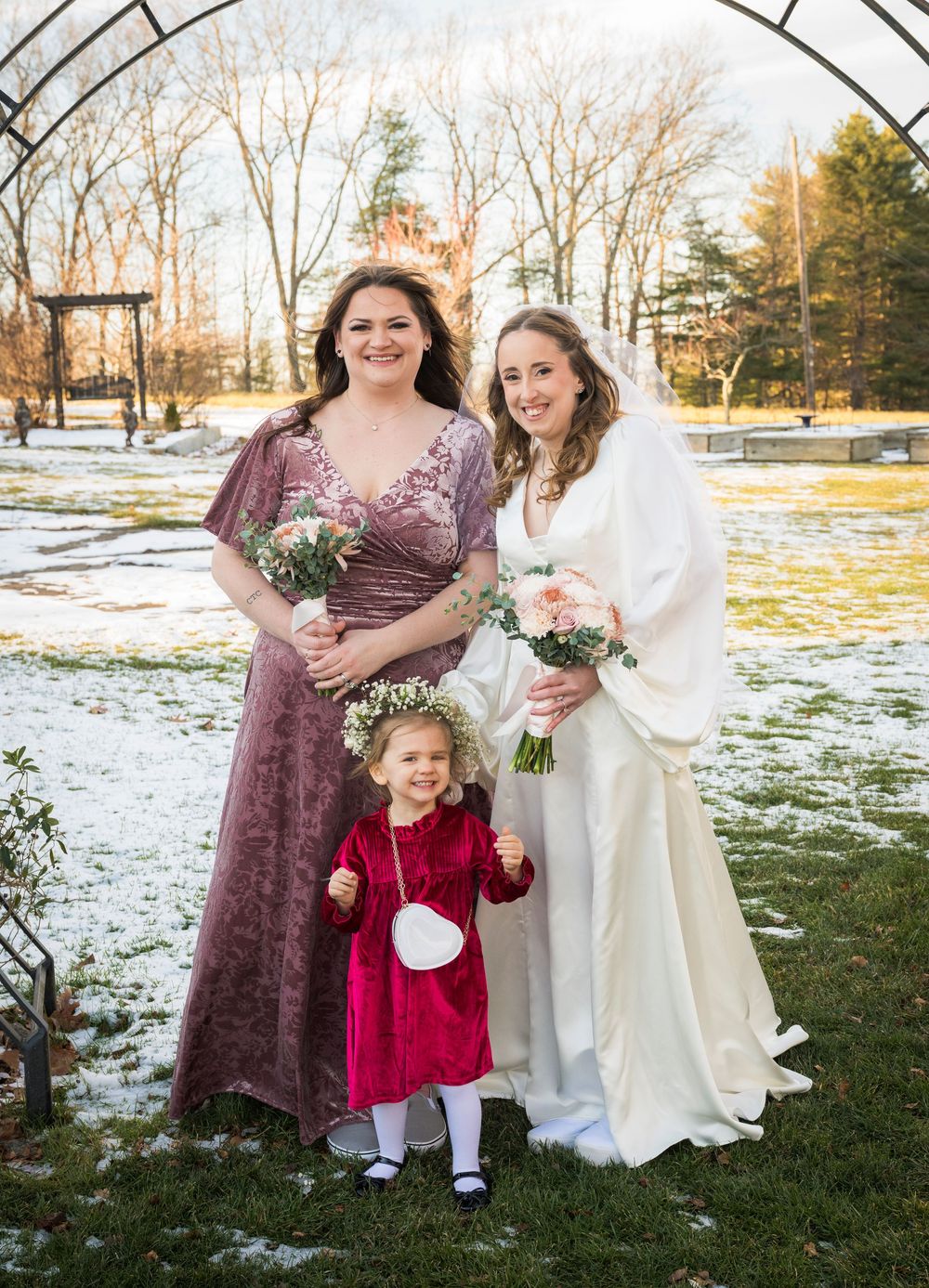 A group in formal attire poses together on snowy grass during a winter wedding photoshoot.