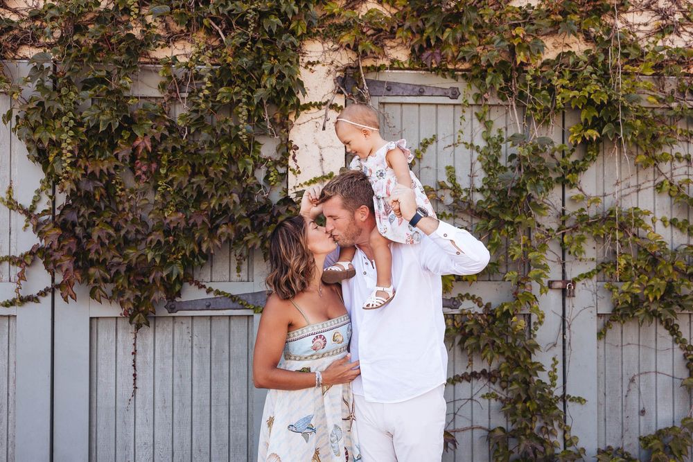Family enjoying a tender moment together against a rustic wall covered in climbing vines.