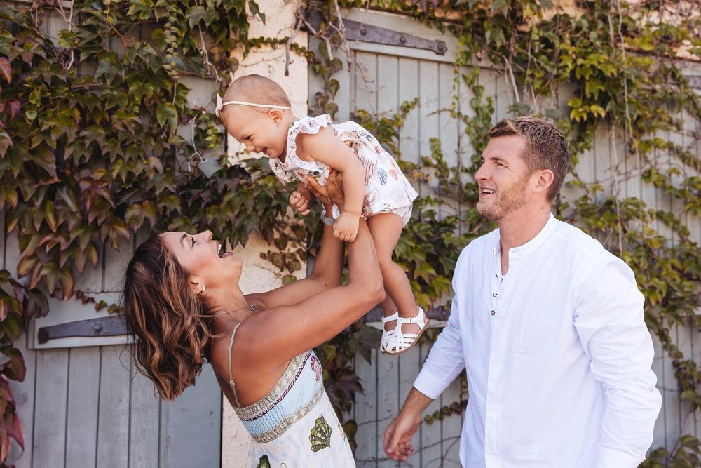 A joyful family moment captured outdoors against a rustic wall with greenery.