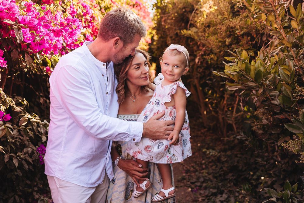 Family embracing in an autumn garden with vibrant pink flowers in the background.