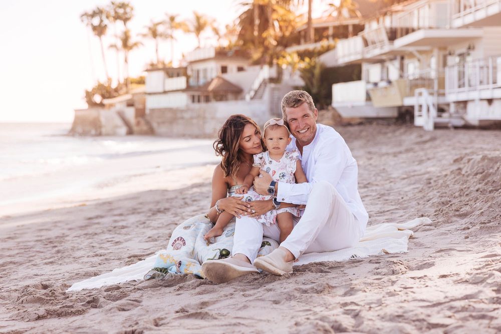 A family enjoys a sunset photo session on a sandy beach with beachfront homes in the background.