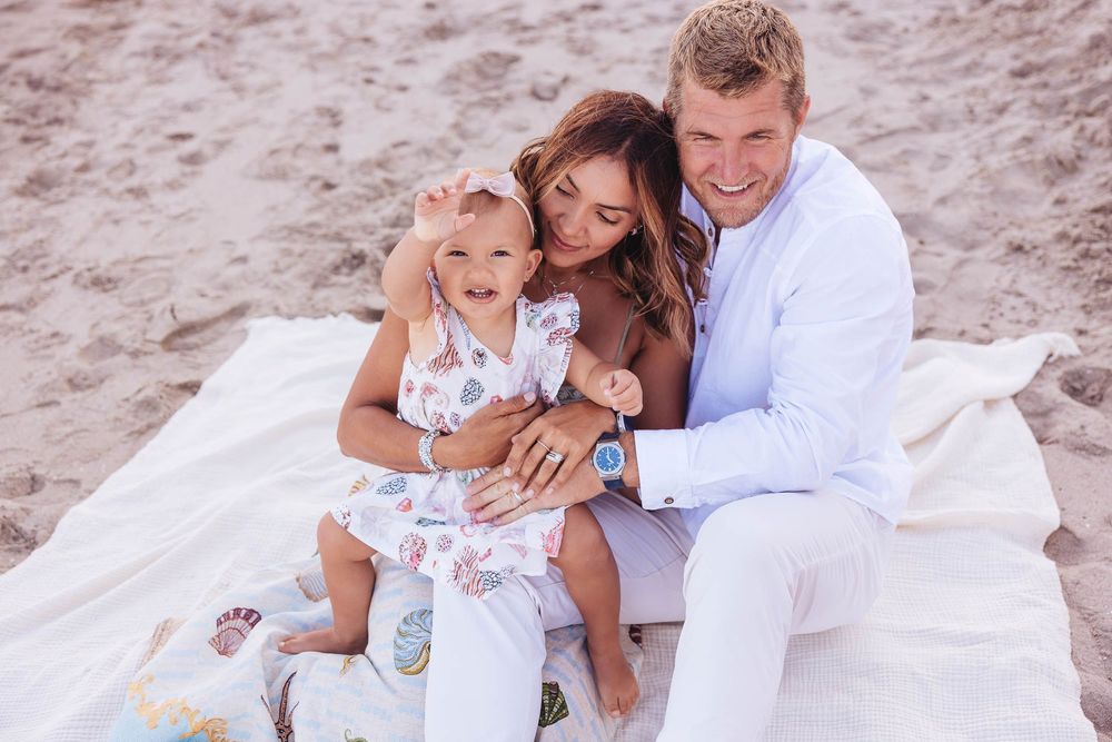 Happy family portrait on beach with white attire in soft lighting.