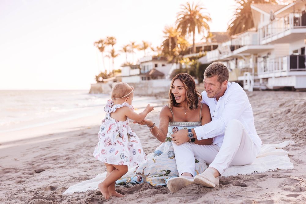 Family enjoying sunset beach photo session with white attire and playful poses on sandy shoreline.