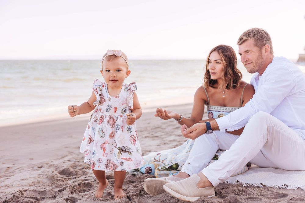 A family in white clothing sitting together on a sandy beach at sunset.