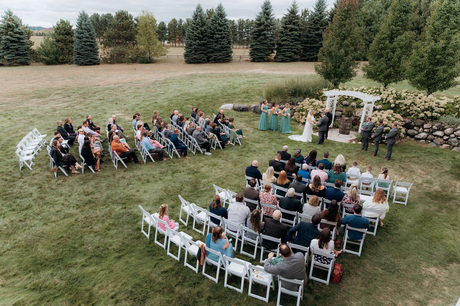 An aerial view of an outdoor wedding ceremony with guests seated in curved rows on a lawn. Garvey Family Wedding Farm in Traverse City MI.