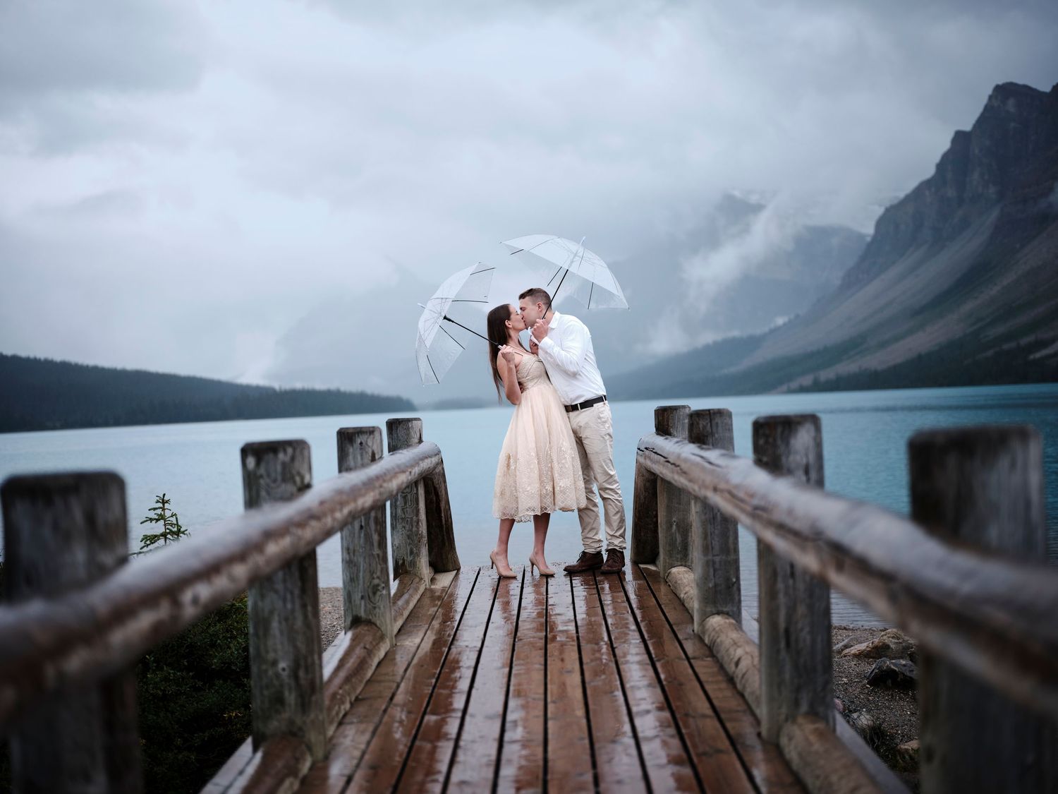 A couple shares a romantic moment on a wooden boardwalk with misty mountains and lake in the background elopement in Banff