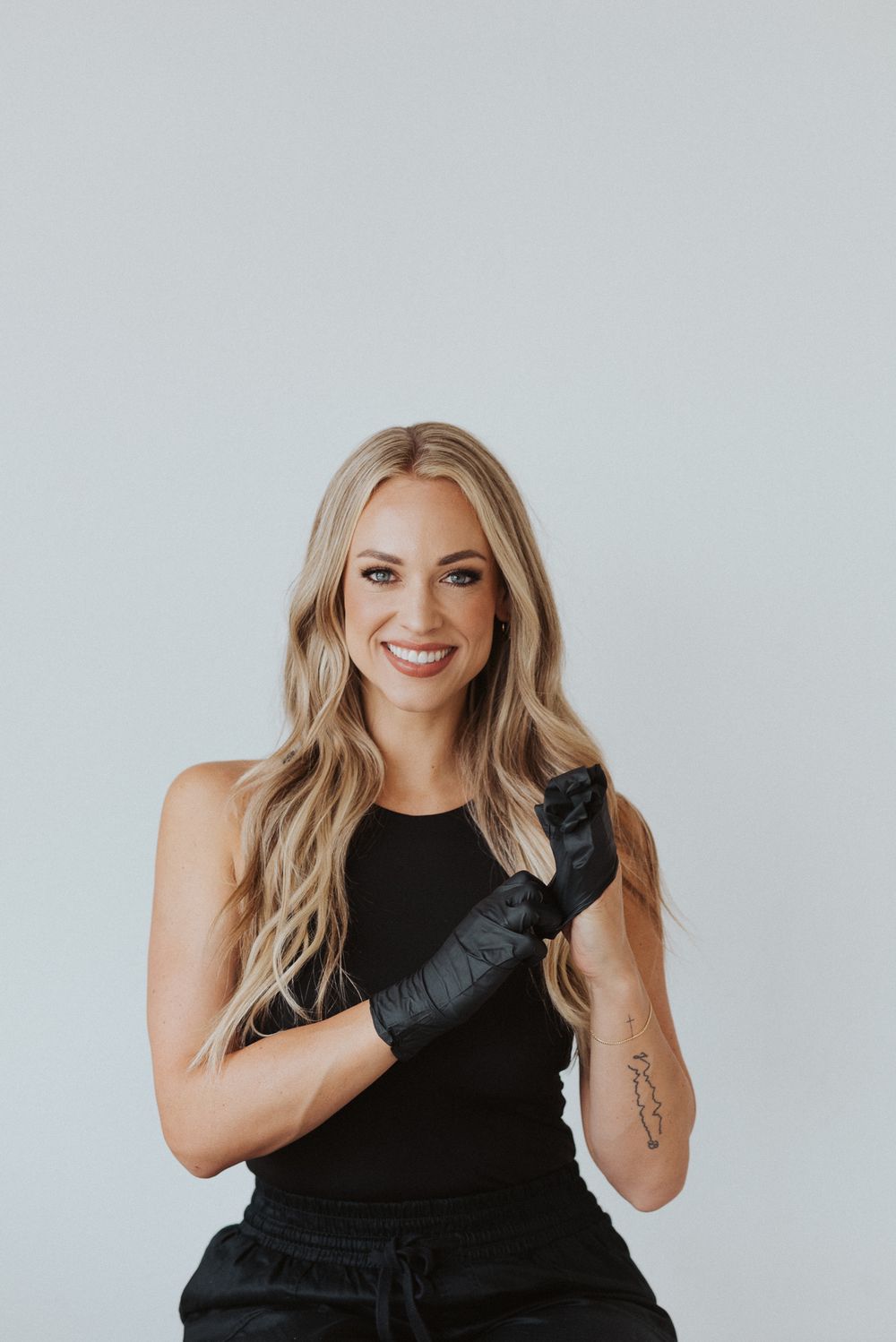 Woman in black tank top smiling during studio photoshoot with minimalist background.