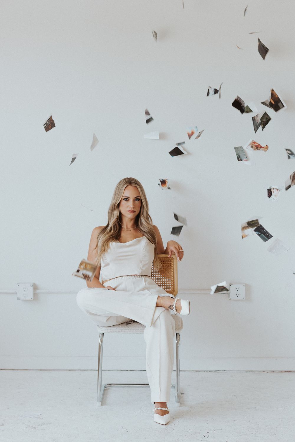 Creative photoshoot with papers flying through air and modern chair against white wall.