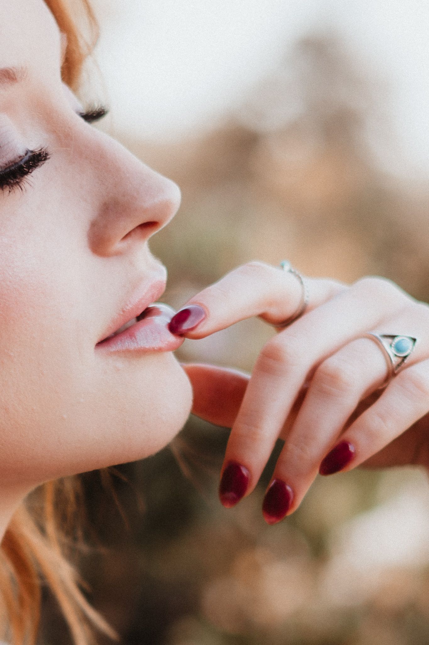 Close up detail of red painted fingernails touching lips in an artistic pose.