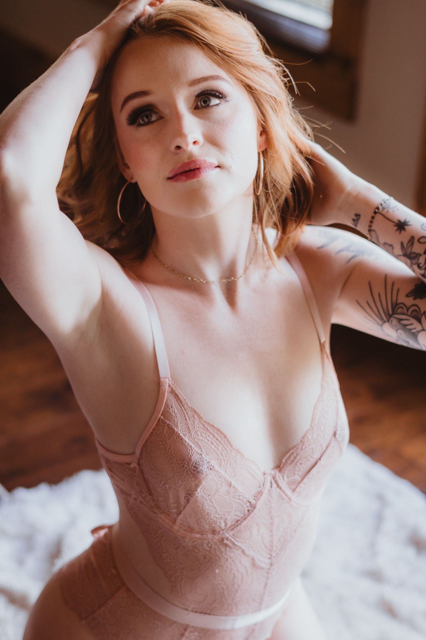 Romantic boudoir photography with soft pink tones and natural window light.
