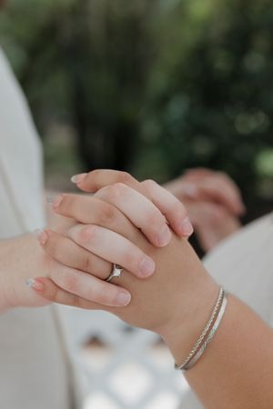 Close-up of hands wearing engagement rings touching tenderly.