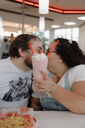 Couple sharing milkshakes and french fries at a retro-style diner.