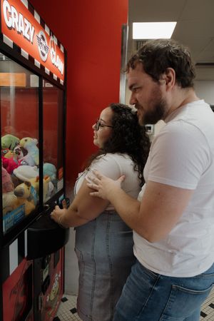 Couple playing at an arcade claw machine with stuffed animals.