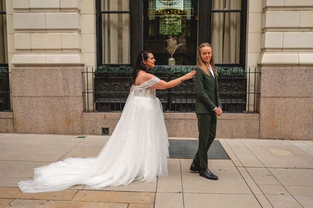 A couple share a first look moment in their wedding attire on a stone patio outside an elegant building.
